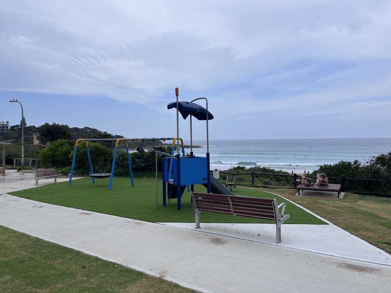 palyground equipment, ench seat, to people liying on a bench, ocean in background
